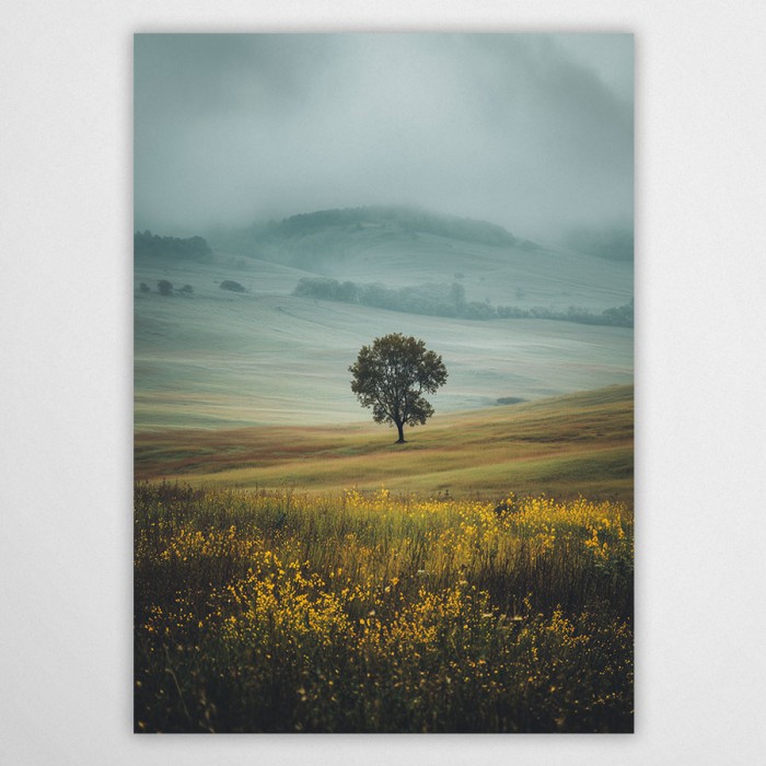 Pejzaż fotograficzny z samotnym drzewem na tle zamglonych, zielonych pagórków i łąki z żółtymi kwiatami. Spokojna i harmonijna kompozycja natury.