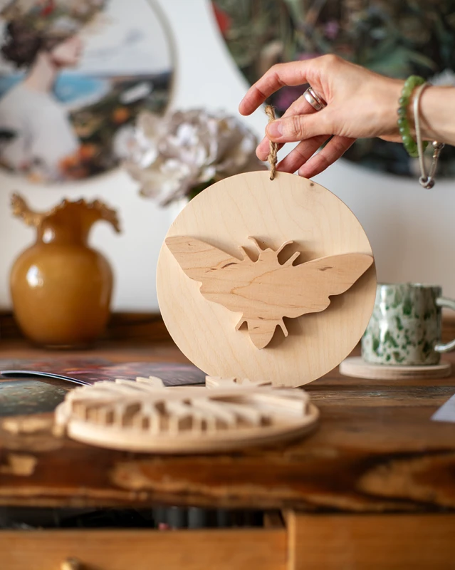 Drewniana dekoracja ścienna w kształcie koła z nałożoną sylwetką ćmy 3D. Rękodzieło wykonane z jasnej sklejki o unikalnym usłojeniu. Produkt zawieszony na naturalnym sznurku. Niepowtarzalny wzór.