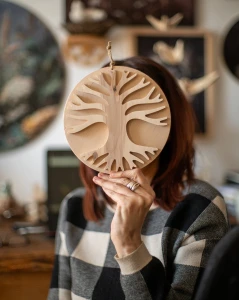 Drewniana dekoracja ścienna w dłoniach przedstawiająca rozłożyste Drzewo Życia 3D. Rękodzieło z jasnej sklejki liściastej o unikalnym usłojeniu, zawieszone na sznurku jutowym. Niepowtarzalny wzór na bazie koła.