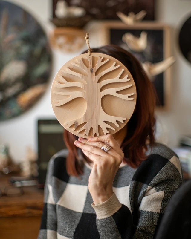 Drewniana dekoracja ścienna w dłoniach przedstawiająca rozłożyste Drzewo Życia 3D. Rękodzieło z jasnej sklejki liściastej o unikalnym usłojeniu, zawieszone na sznurku jutowym. Niepowtarzalny wzór na bazie koła.